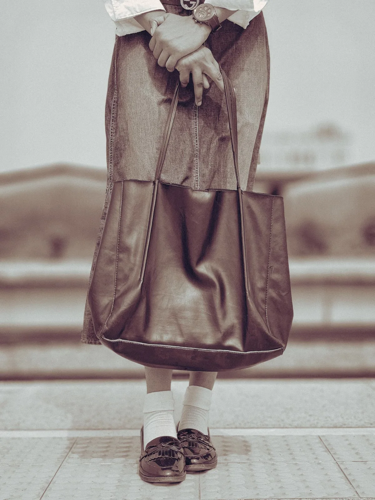 A person carrying a large leather tote — for wholesale buyers importing leather bags from China, the bag's declared customs value and correct HS code classification determine the duty rate applied at the port of entry