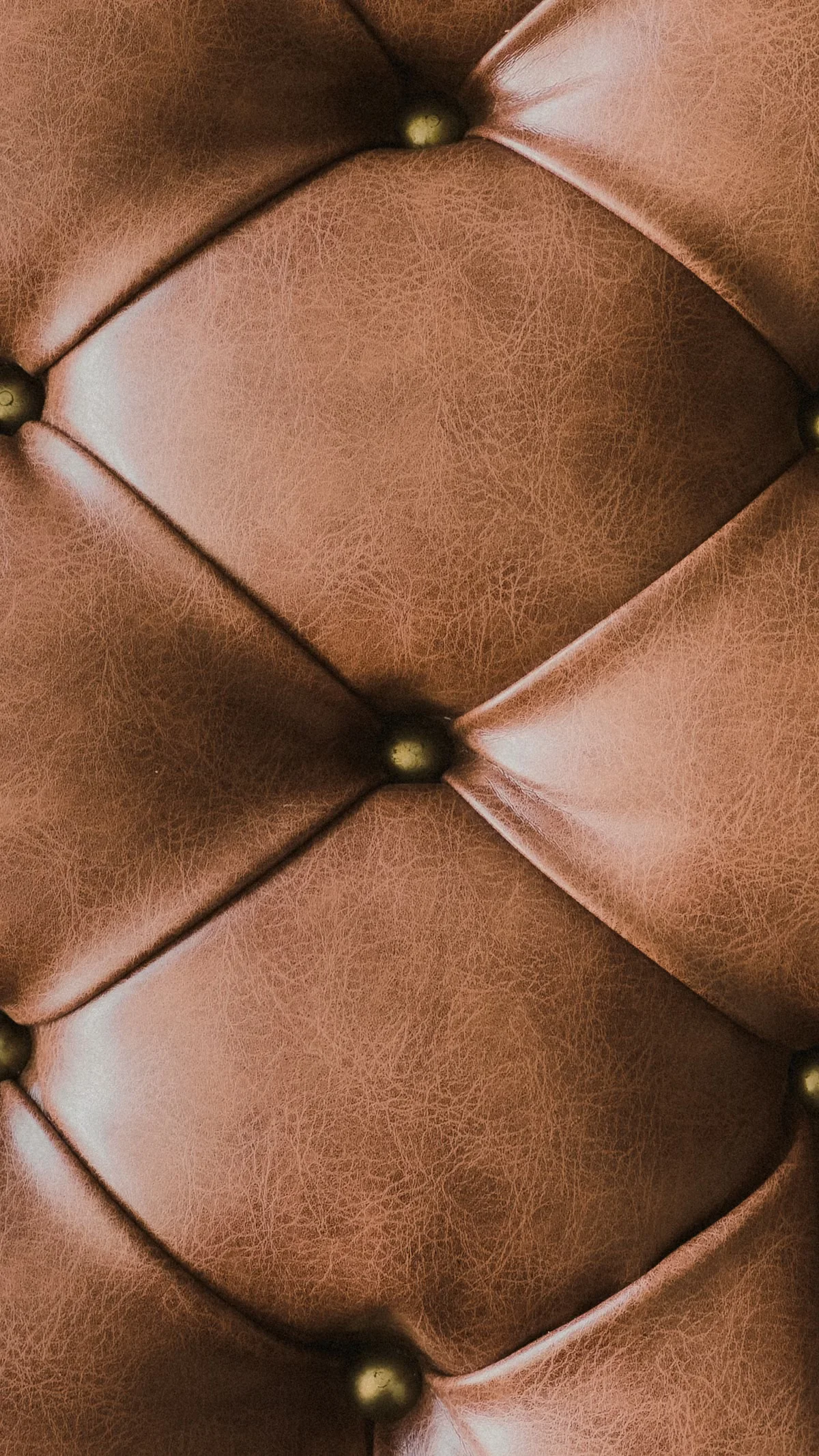 Tan leather upholstery with classic diamond quilting and antique brass nail-head studs — the combination of leather color, stitch pattern and hardware finish creates the complete aesthetic register that defines a bag's market positioning