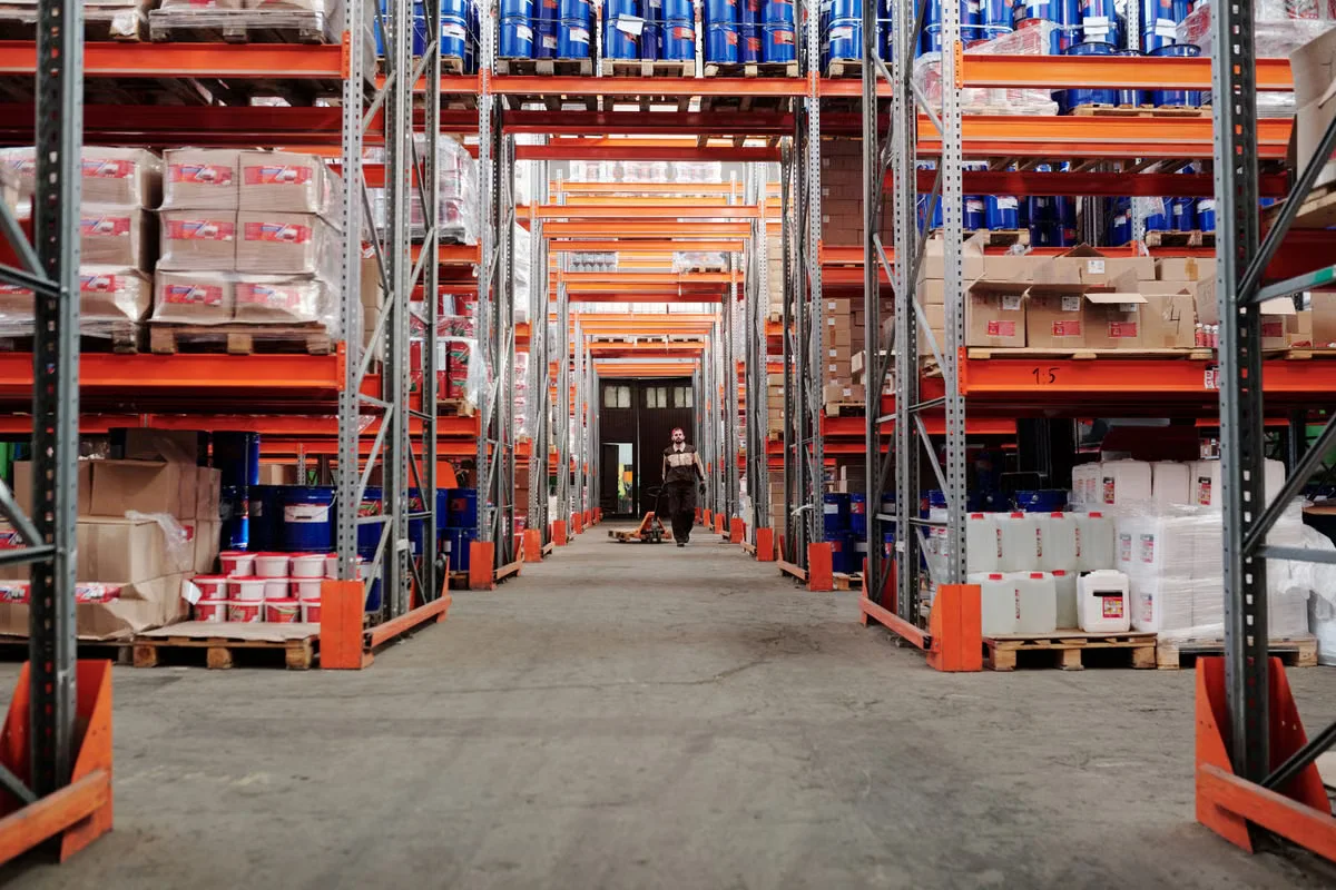 Bulk warehouse fulfillment center with floor-to-ceiling racking systems and pallet jacks — represents the scale of inventory management involved in wholesale leather bag sourcing and minimum order fulfillment