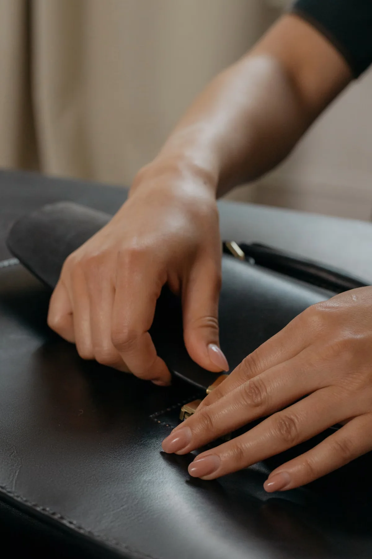Close-up of hands opening the clasp of a black leather briefcase — representing the hardware function testing that should be performed on every leather bag sample before production approval