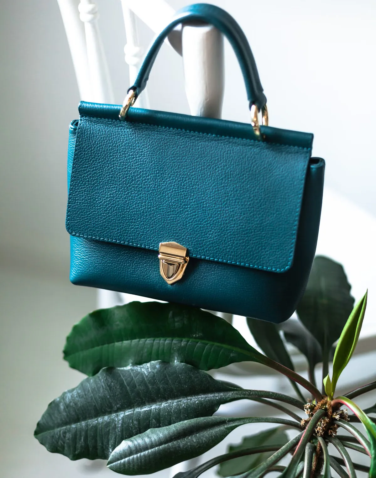 A structured teal leather top-handle bag hung over a white chair back — clear visual representation of the kind of finished product that a complete tech pack makes consistently reproducible across production runs