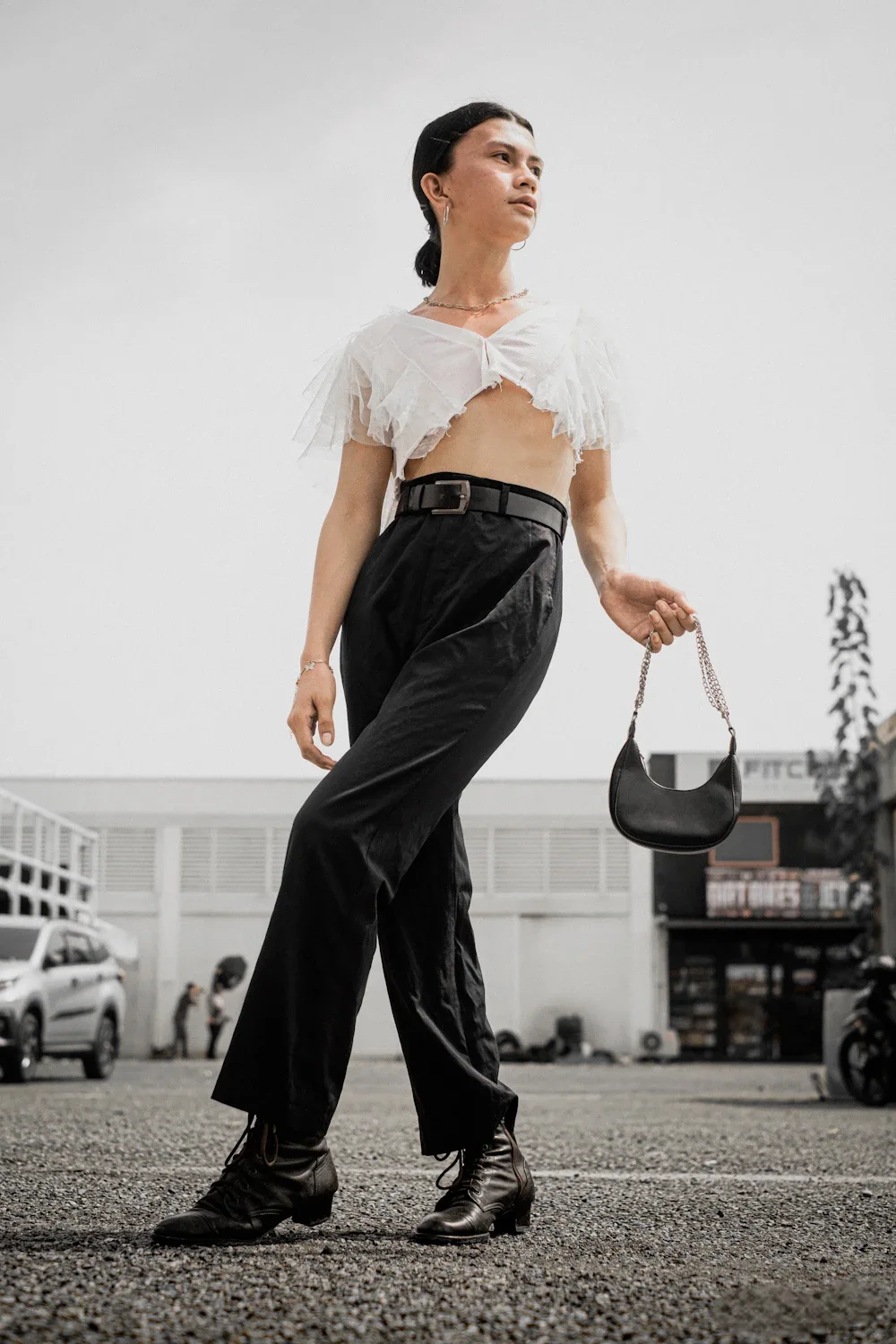 A model carrying a small black crescent moon bag, styled with wide-leg trousers — the silhouette worn naturally at the side