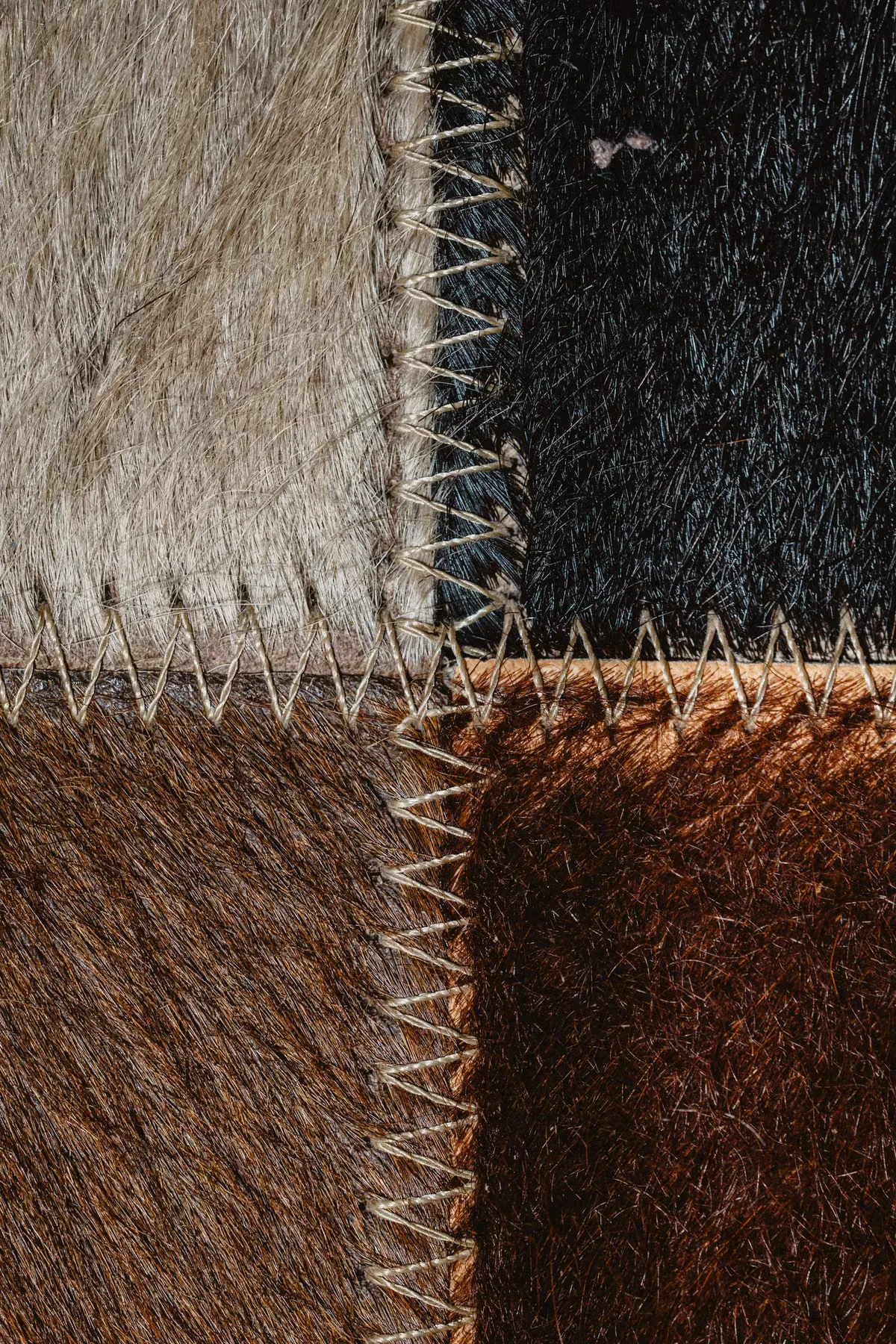 Patchwork of genuine leather hides in contrasting colors — white, black, and cognac — showing the natural variation, hair texture and hand-sewn seams that characterize real animal leather versus the uniform surface of vegan alternatives